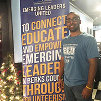 Emerging Leaders United member in Emerging Leaders United shirt in front of mission sign