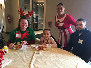 Emerging Leaders United volunteers smiling in holiday apparel with kids at the Santa's Workshop event