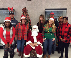 Smiling volunteers in holiday apparel with Santa in the middle
