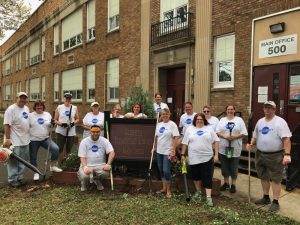Group of volunteers in matching Day of Caring shirts holding gardening tools at Glenside elementary