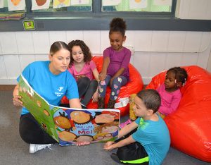YMCA students sitting together reading a large book with teacher