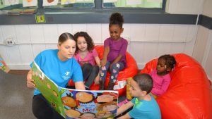 YMCA students sitting together reading a large book with teacher