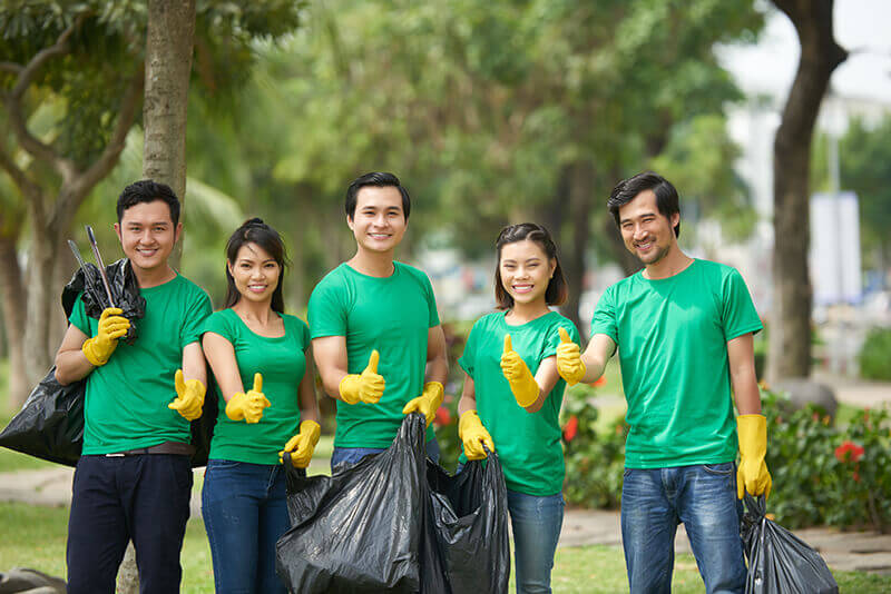 Volunteers in matching green shirts smiling and giving a thumbs up while collecting trash