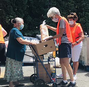 A volunteer in an orange vest is loading food into the cart of an older woman