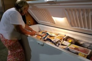 A woman is reaching into a chest freezer full of frozen vegetables and meats