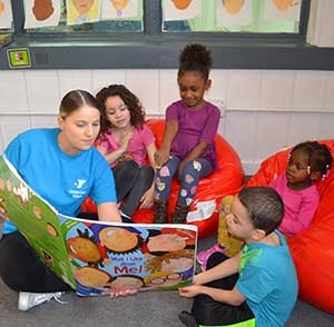 A female child care teacher is reading an oversized book to four children