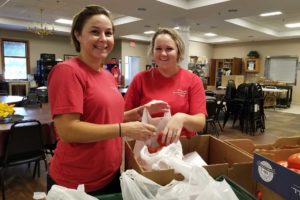 Two women wearing red shirts are packing food for a food distribution in the Boyertown area