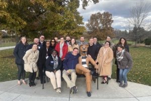A group of men and women wearing winter coats and posing outside. The group is at Penn State Berks and they are posing with a statue of the Nittany Lion