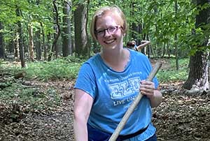 A woman in a blue shirt is smiling while holding a rake at Nolde Forest