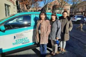 An SUV wrapped with the Street Medicine and Tower Health logos. Three women are standing in front of the SUV. They are wearing winter coats and smiling
