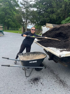 A woman is shoveling mulch from the back of a pickup truck