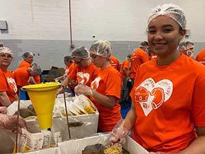 A young woman wearing a bright orange shirt and a hair net is smiling