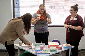 A woman is organizing children's books and games on a table while two other women watch