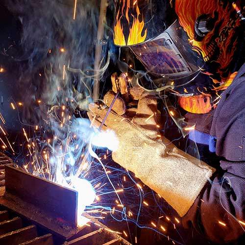 A welder wearing protective gear is welding a piece of steel