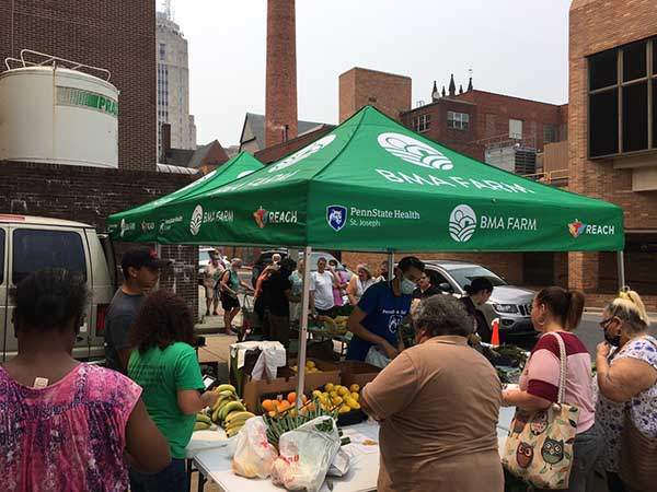 A group of people are shopping at an outside food stand in the City of Reading offering fresh fruits and vegetables