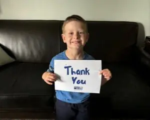 A little boy is smiling happily and holding a sign that says "thank you"