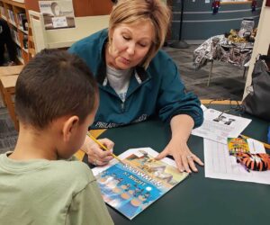 A woman and an elementary-school-aged boy are in a library. They are both looking at a book
