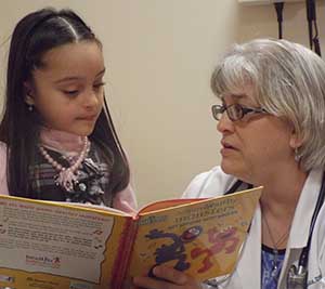 A girl reads a book while her doctor listens