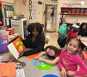 A teen girl is holding a book while two elementary-aged girls smile at the camera
