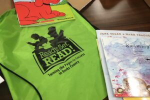 A green drawstring bag with the Ready.Set.READ! logo is lying on a table. Two books are resting on the corners of the bag