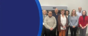 A group of men and women in a conference room are smiling at the camera