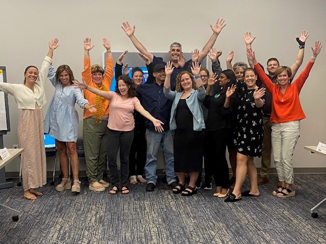A boy is standing in a classroom. He is holding a stack of books and smiling