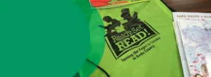 A green sling bag with the Ready.Set.READ! logo. The sling bag is next to a book