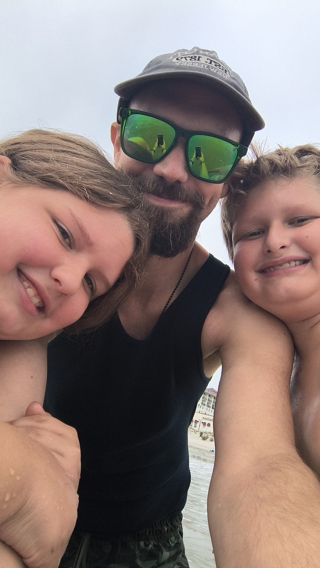 Literacy Council graduate Doug Dimmig smiling on the beach in sunglasses and a hat during a selfie with his two children.