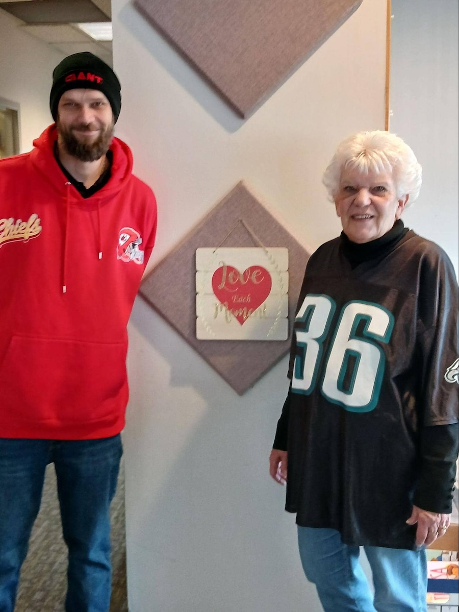 Adult learner Doug wearing a red Chiefs hoodie standing next to a smiling woman in an Eagles jersey at a Literacy Council event.