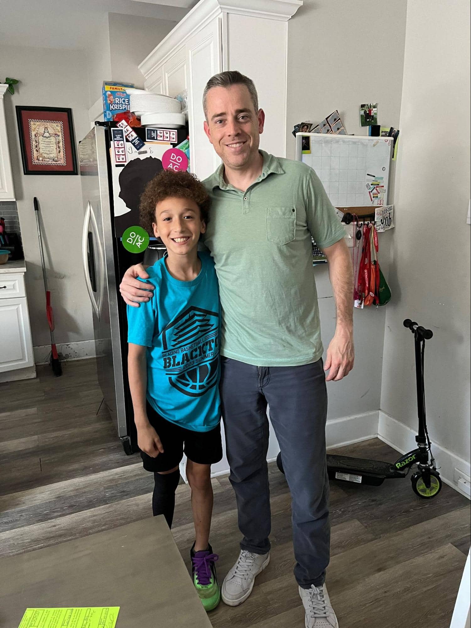Big Brothers Big Sisters of Berks County PA participants Greg and Jacob smiling together in a kitchen, with Jacob wearing a blue basketball shirt.