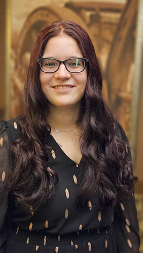 A woman with long hair and glasses is smiling at the camera