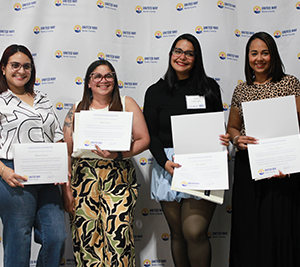 Four women are standing in front of the United Way step and repeat. They are each holding a certificate and smiling at the camera
